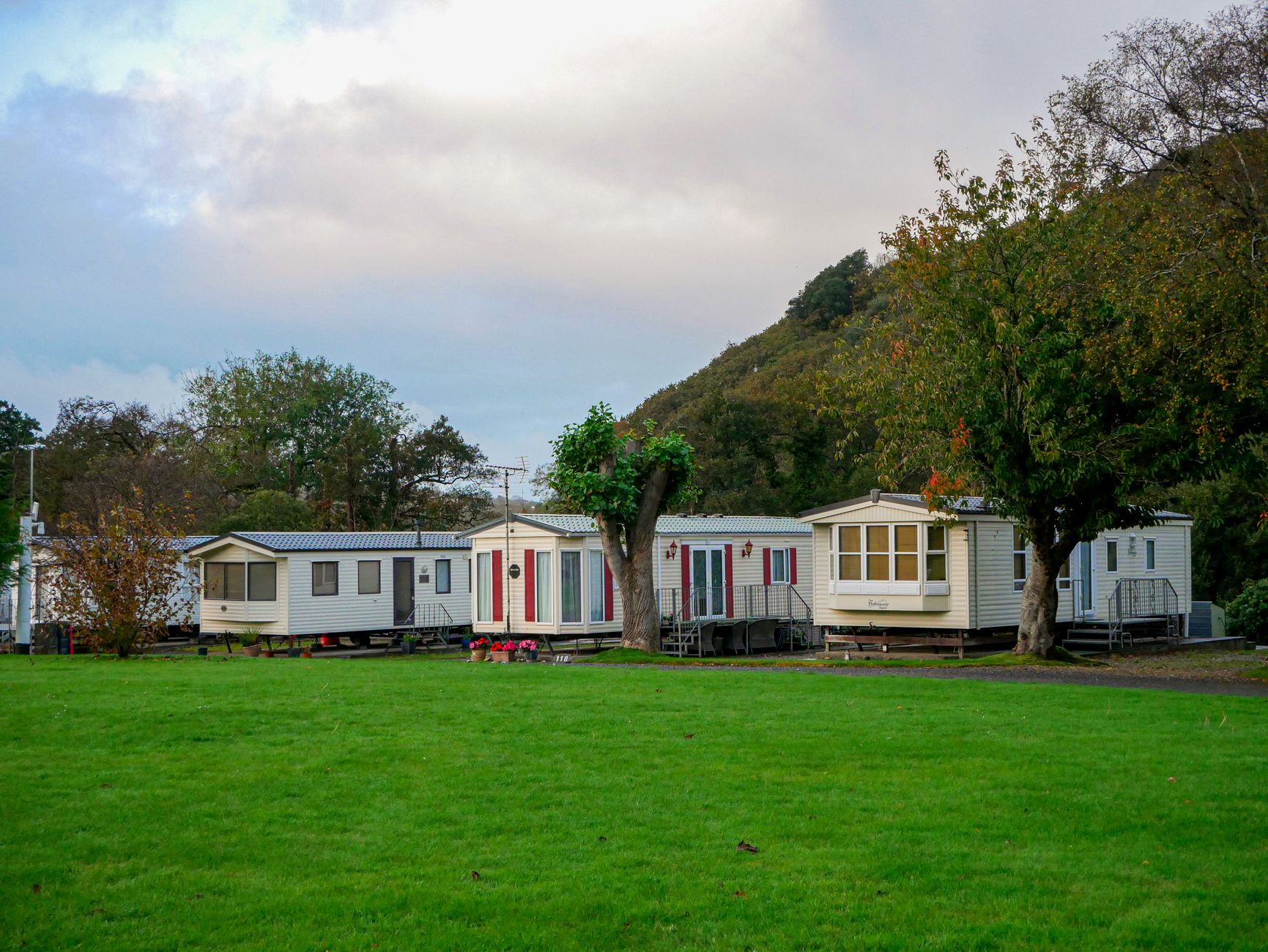 Row of static caravans on grass with trees and hills in background at a holiday park