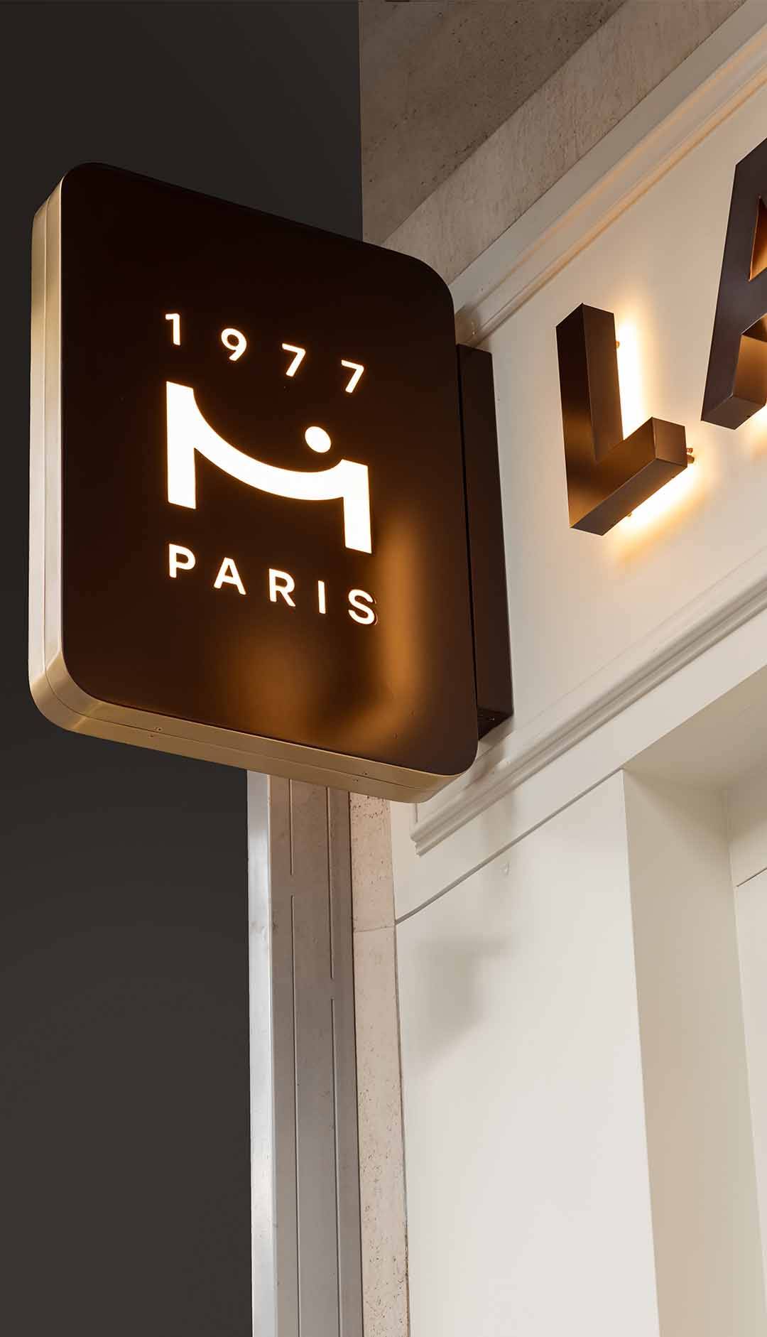 Enseigne lumineuse avec logo stylisé et texte '1977 PARIS'