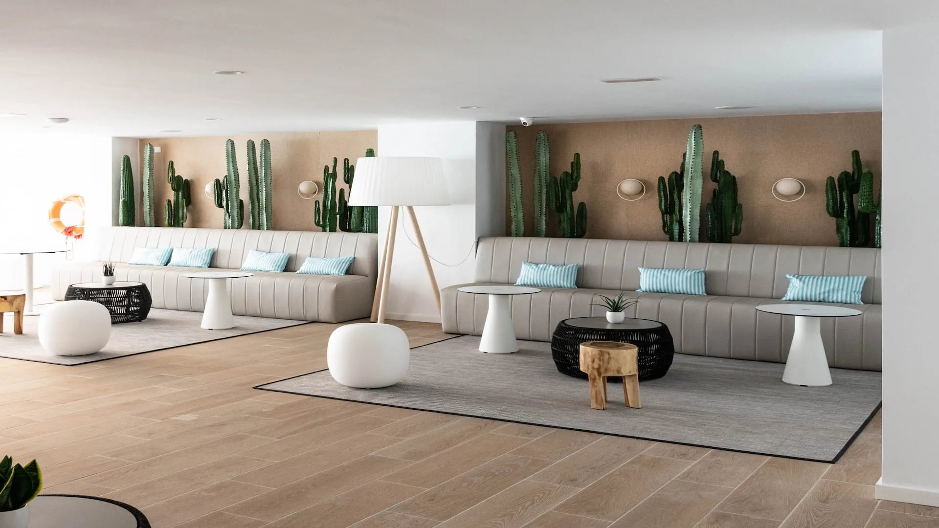 Recepción de hotel con sofás grises, cactus decorativos y lámparas blancas