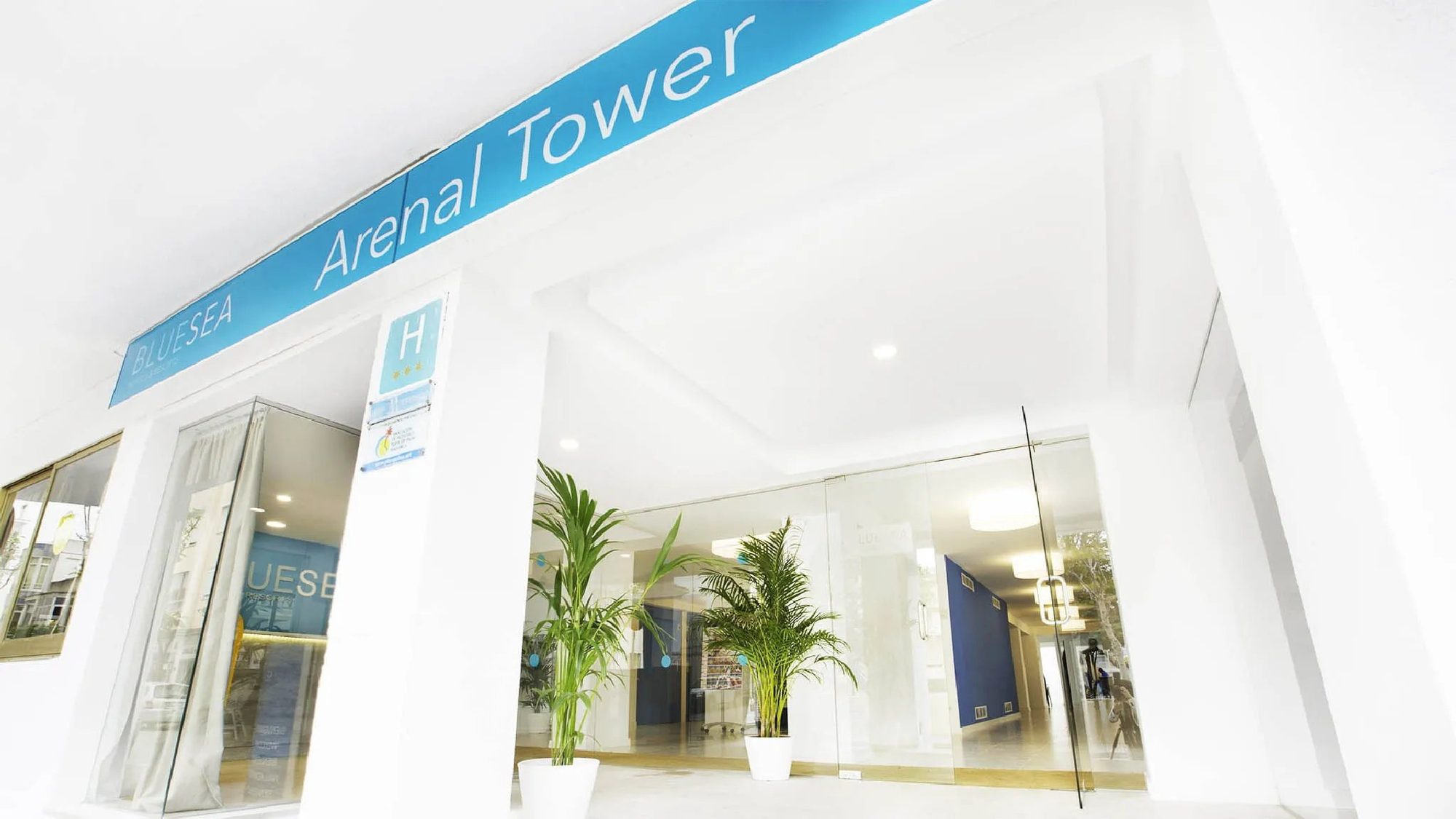 Entrada moderna de hotel con letrero azul Arenal Tower y puertas de cristal