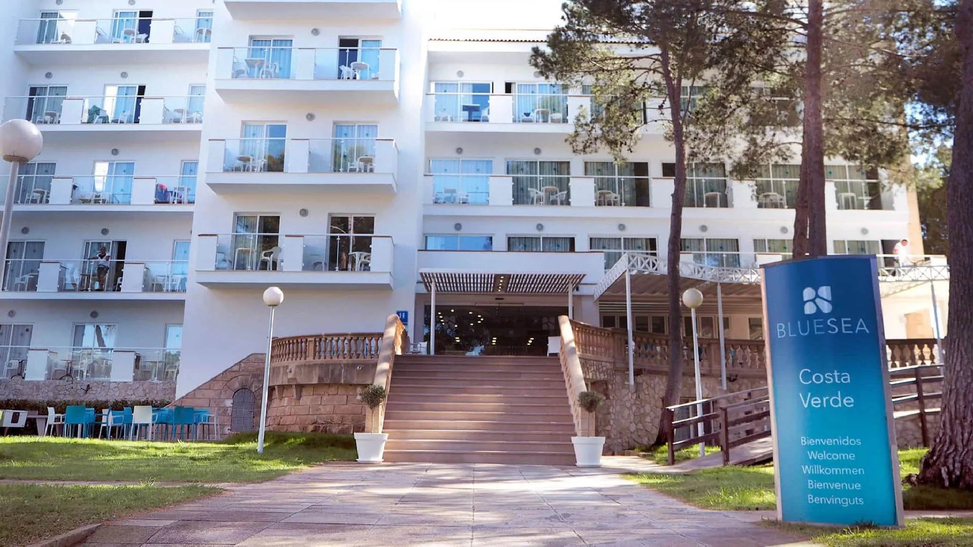 Fachada blanca de hotel resort con balcones, escaleras de acceso y cartel de bienvenida Costa Verde